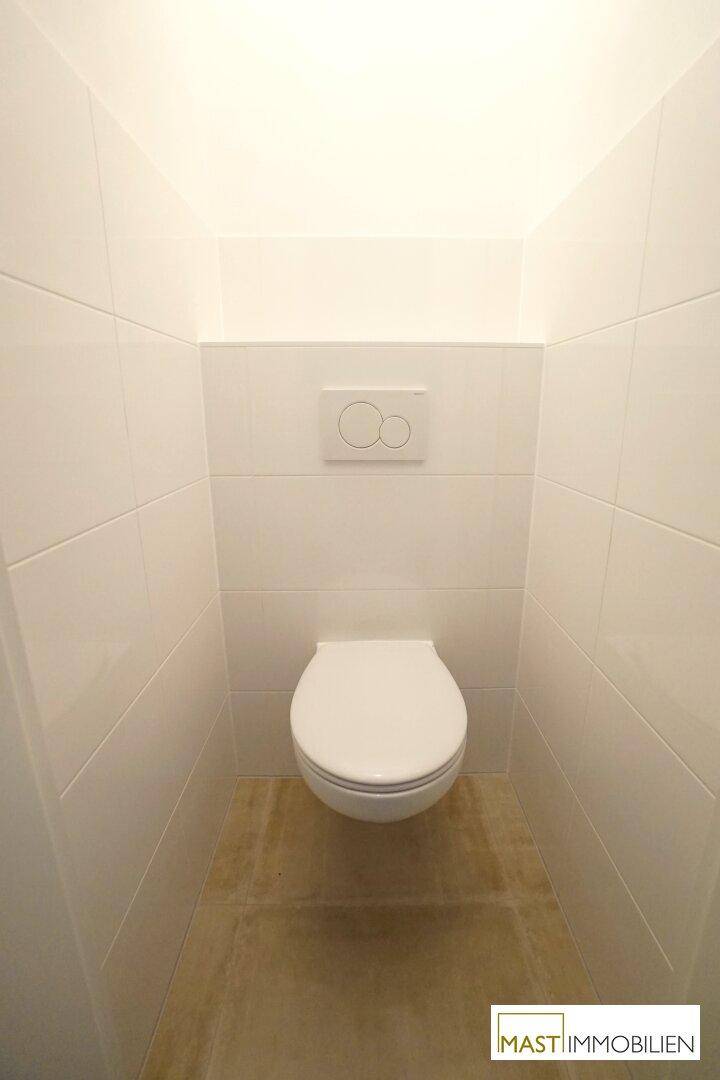 Separates WC mit wandhängender Toilette und weißen Fliesen an den Wänden.