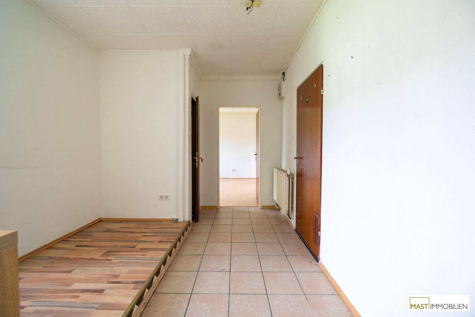 Flur mit gemischtem Fliesen- und Laminatboden, der zu weiteren Räumen führt und einen Bettrahmen zeigt.