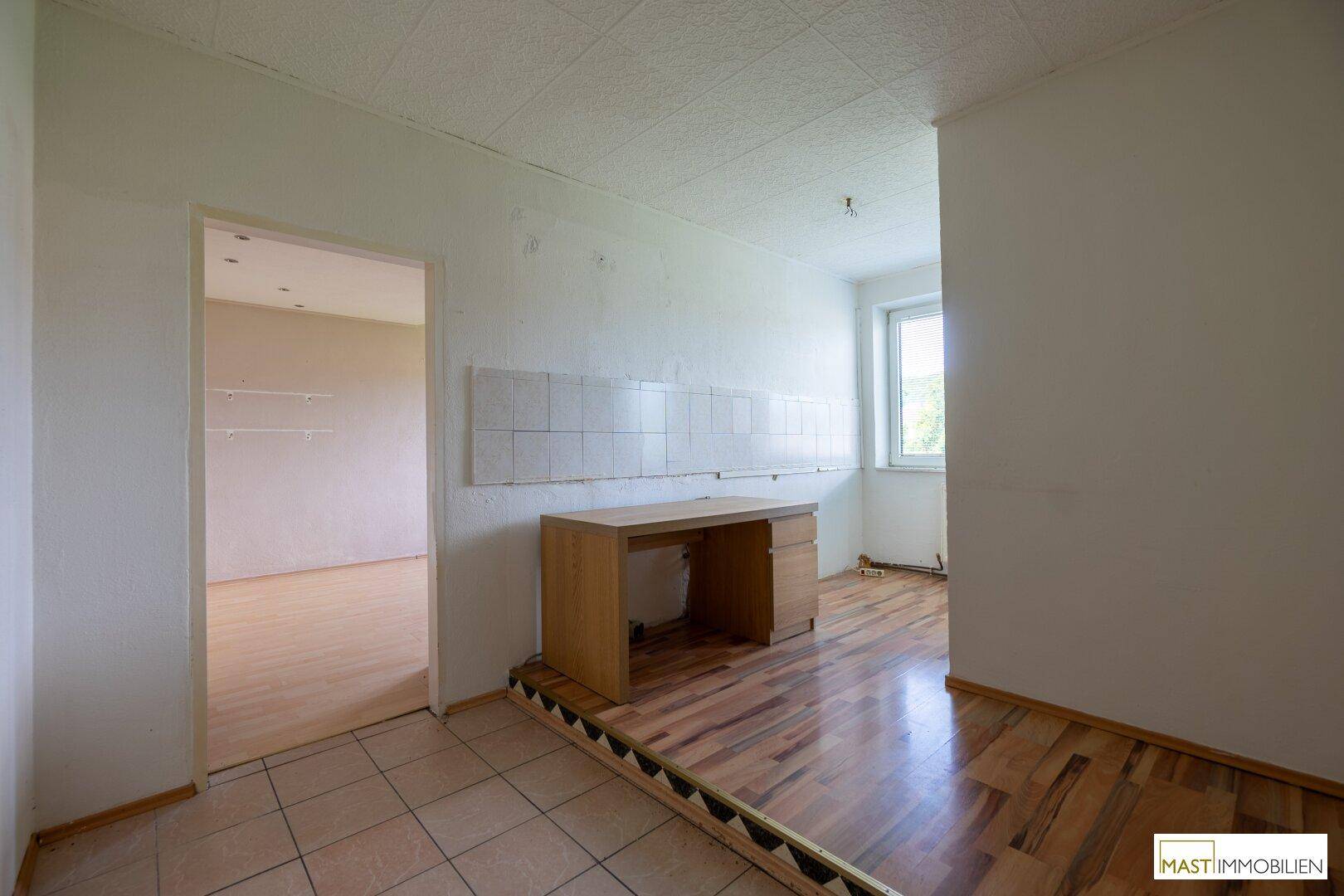 Raum mit einem Schreibtisch, gefliester Wand und Holzboden, der einen Durchgang zu einem weiteren Zimmer bietet.
