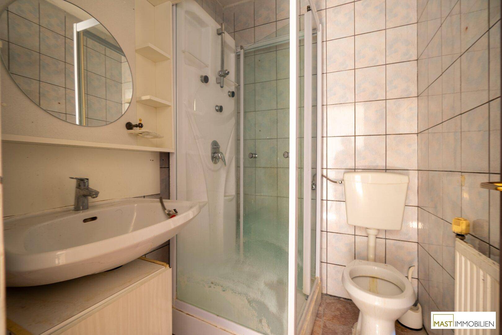 Badezimmer mit Dusche, Waschbecken und Toilette, ausgestattet mit hellen Fliesen und einem Spiegel.