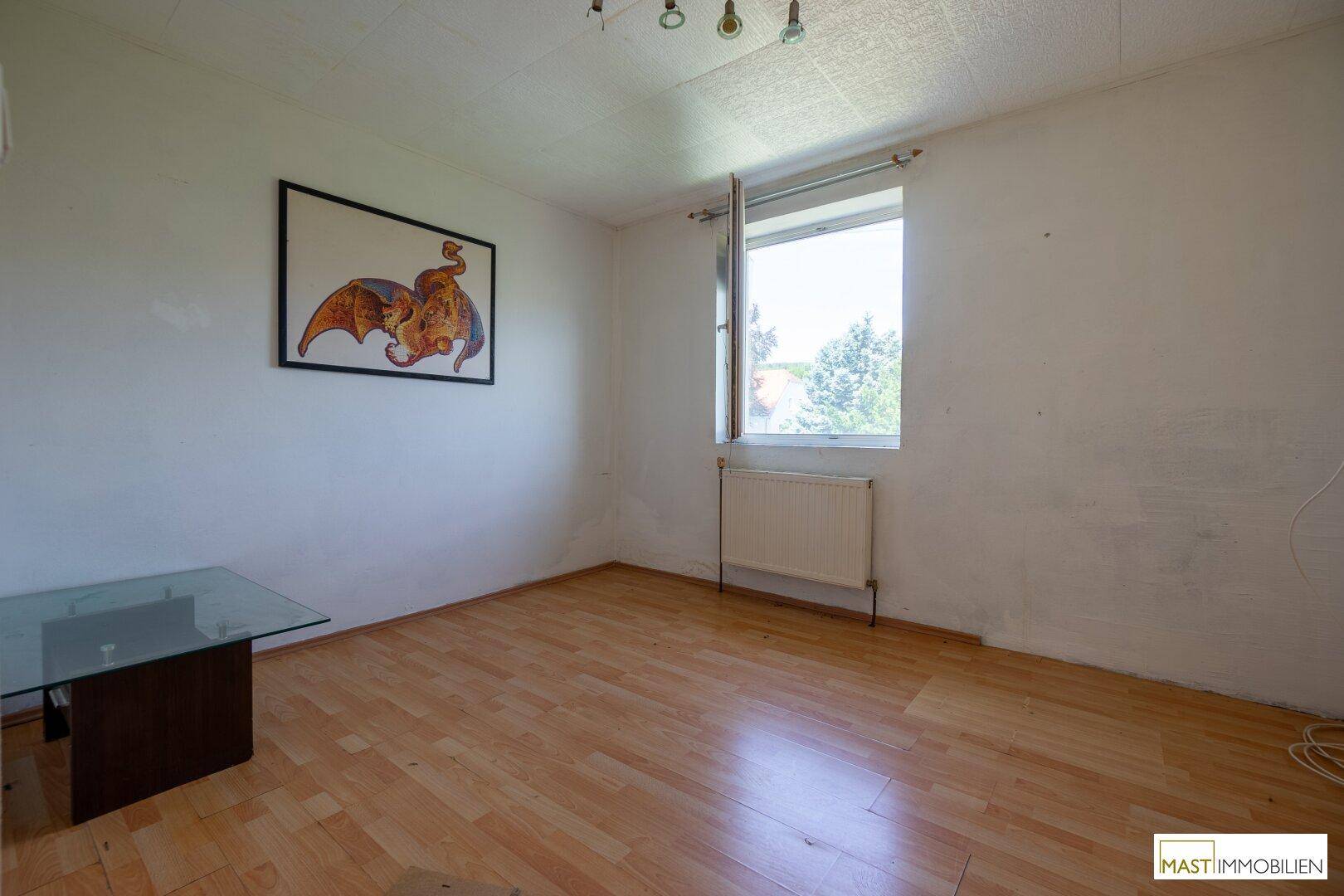 Heller Raum mit Laminatboden, weißen Wänden und einem Fenster, das den Blick nach draußen ermöglicht.