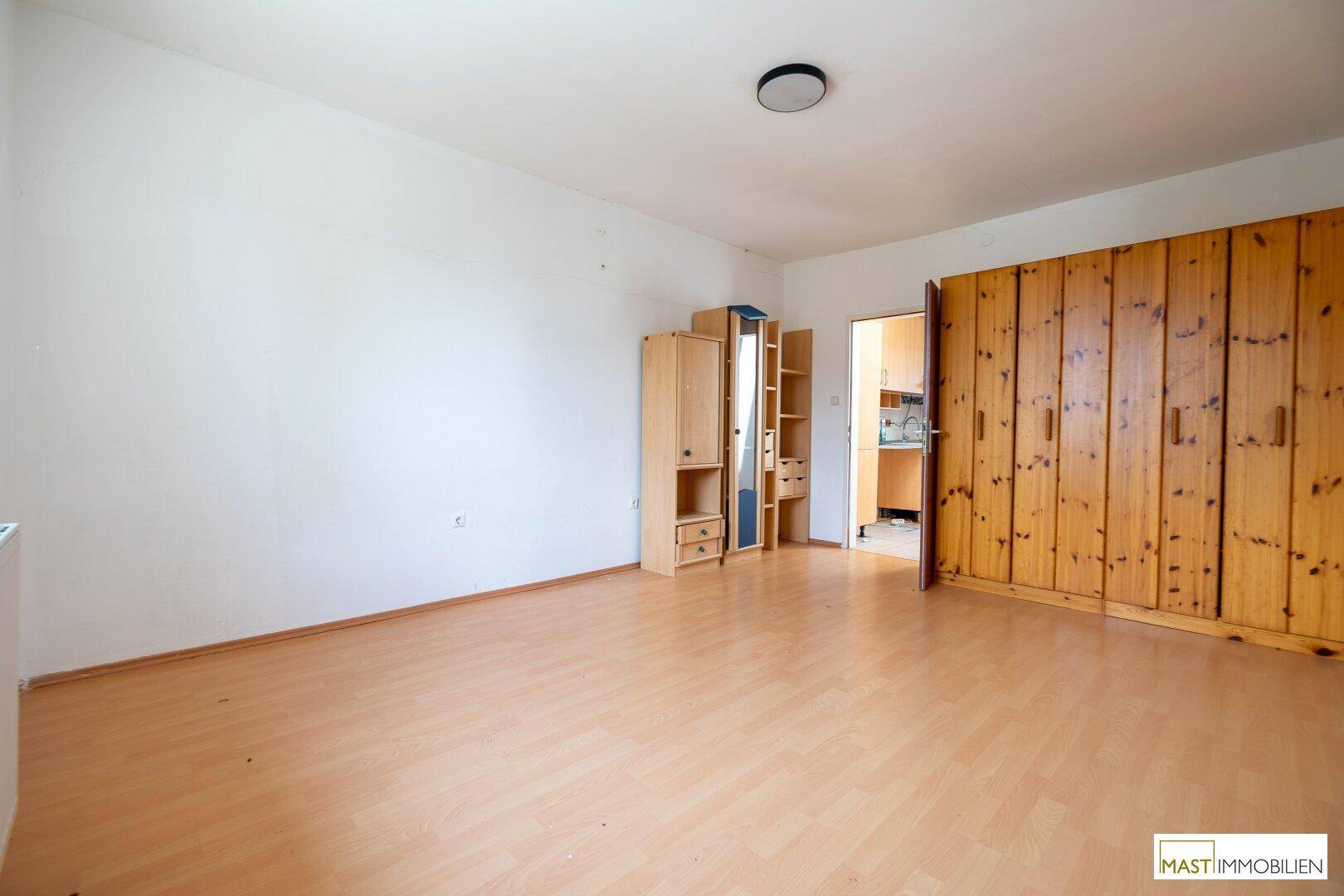 Geräumiger Raum mit hellem Laminatboden und einem großen Holzschrank, der viel Stauraum bietet.