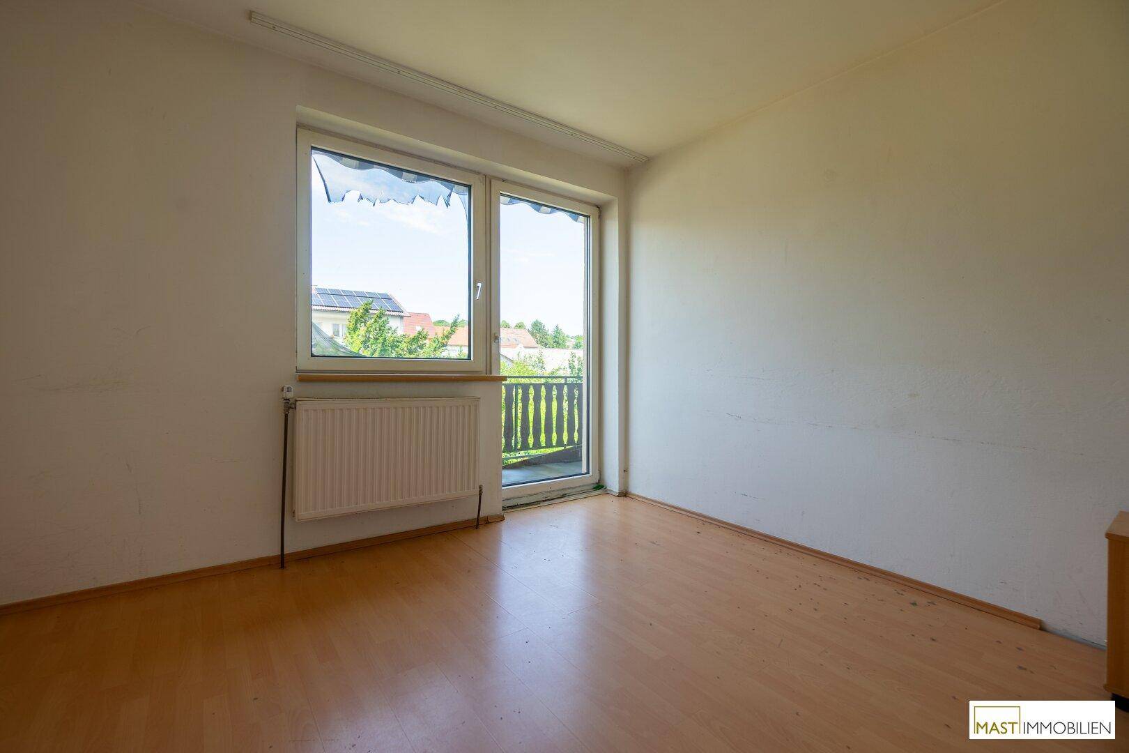 Leeres Schlafzimmer mit Laminatboden und Zugang zu einem kleinen Balkon mit Aussicht.