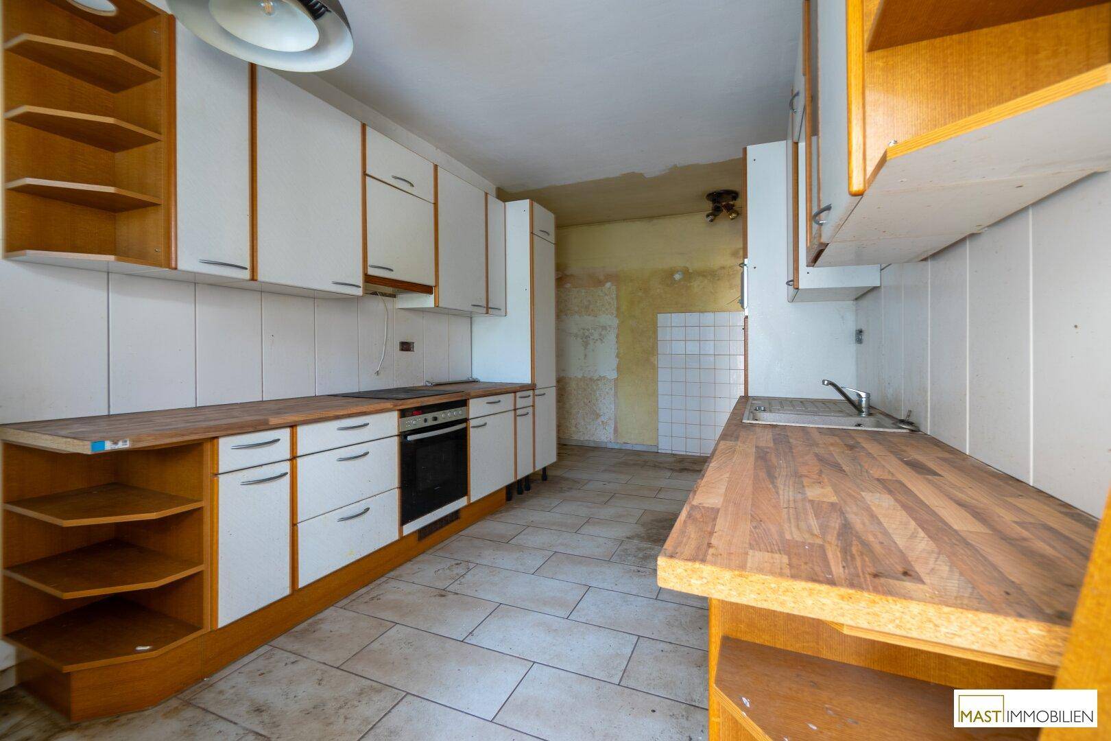 Ältere Einbauküche mit Holz- und weißen Schränken, bereit für eine umfassende Renovierung.