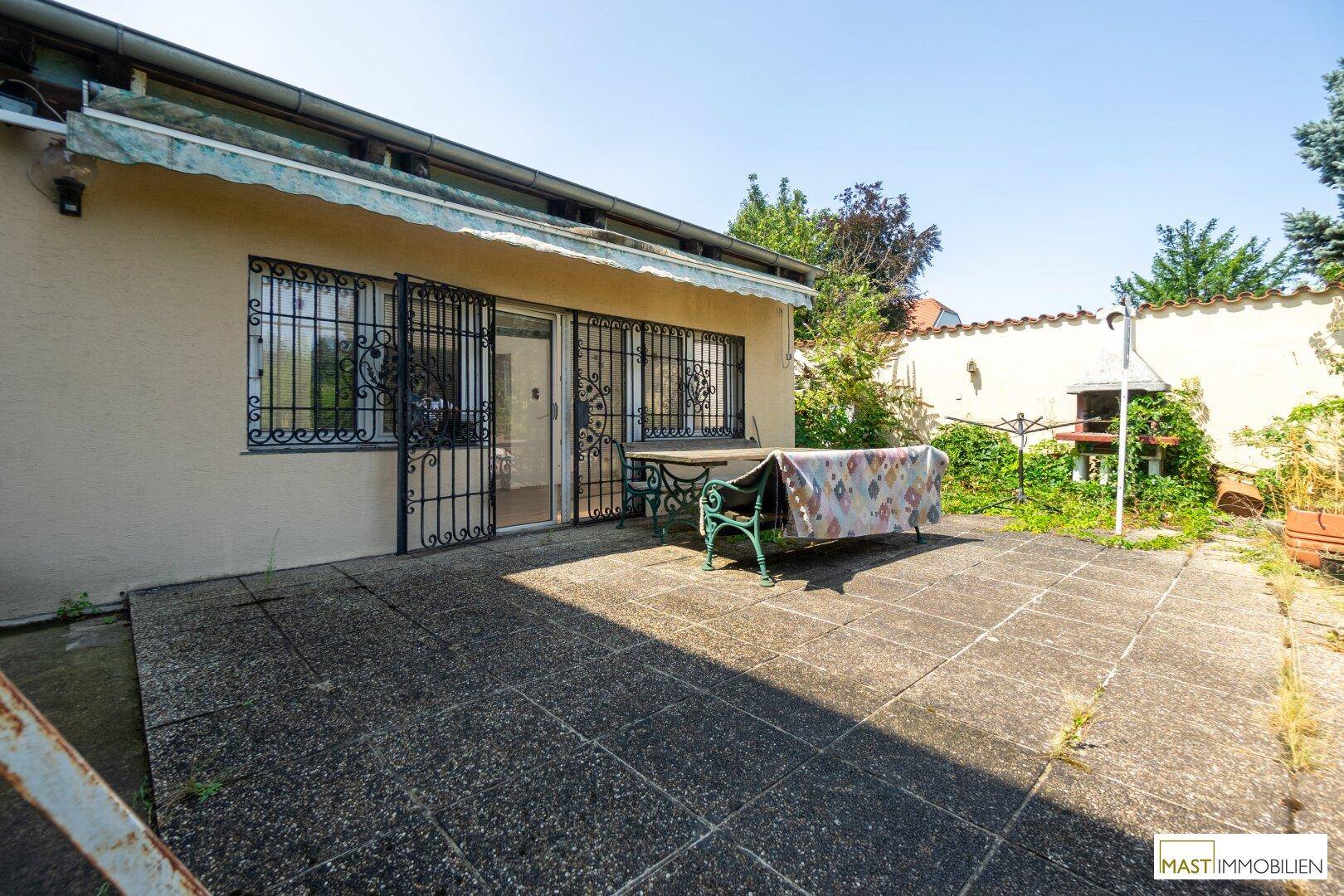Große gepflasterte Terrasse mit Gartentisch und einem gemauerten Grillbereich im Freien.