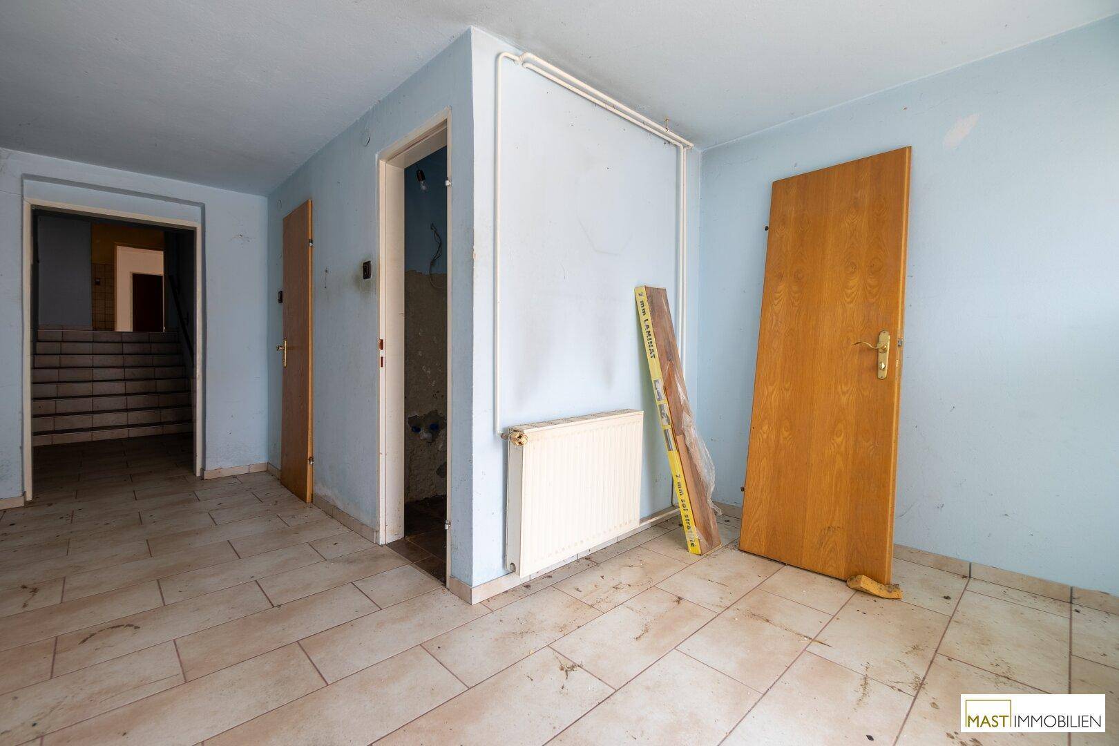 Geräumiger Flur mit hellblau gestrichenen Wänden und Fliesenboden, führt zum Treppenhaus.