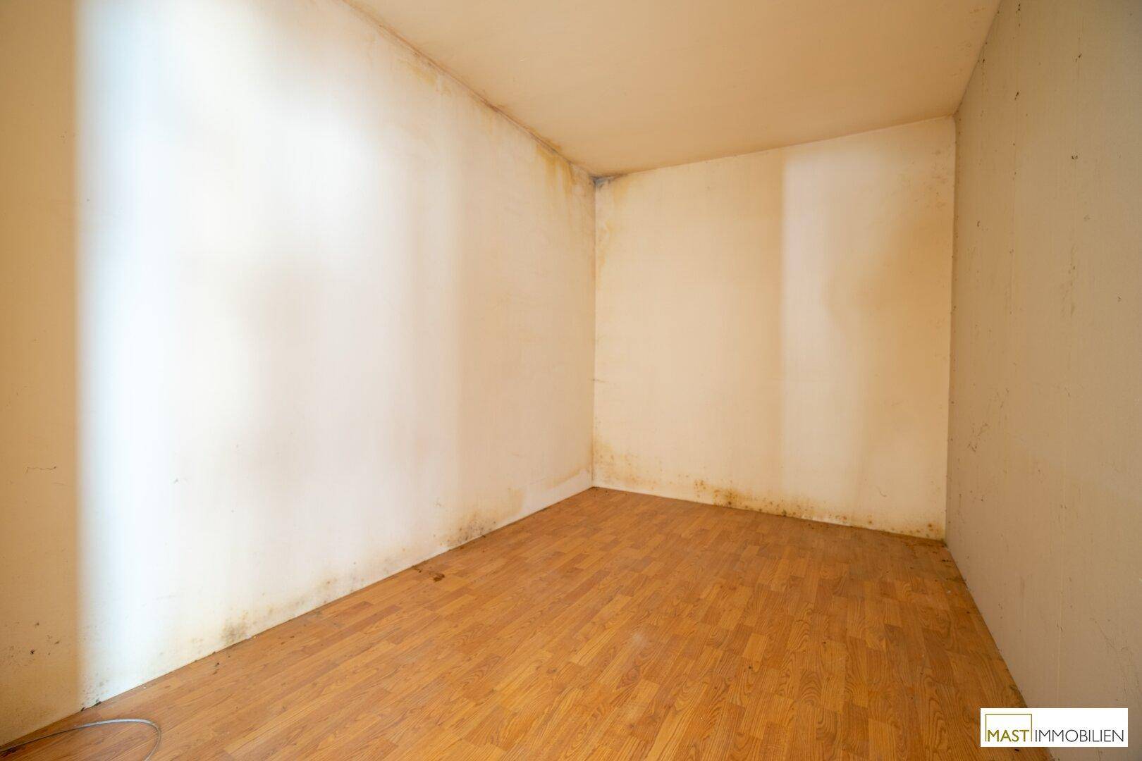Leerer Raum mit Laminatboden und sichtbaren Feuchtigkeitsspuren an den Wänden.