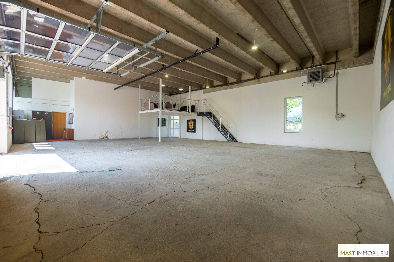 Geräumige Lagerhalle mit Betonboden, hohen Decken und einer integrierten Galerieebene.