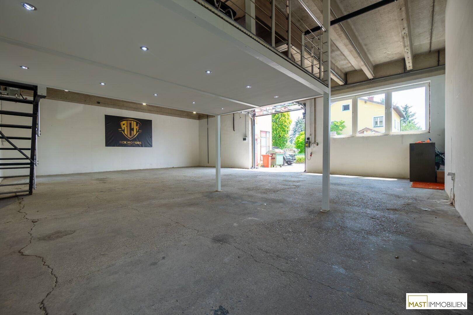 Lagerhalle mit Betonboden, hohen Decken und einer erhöhten Galerie mit Blick nach draußen.