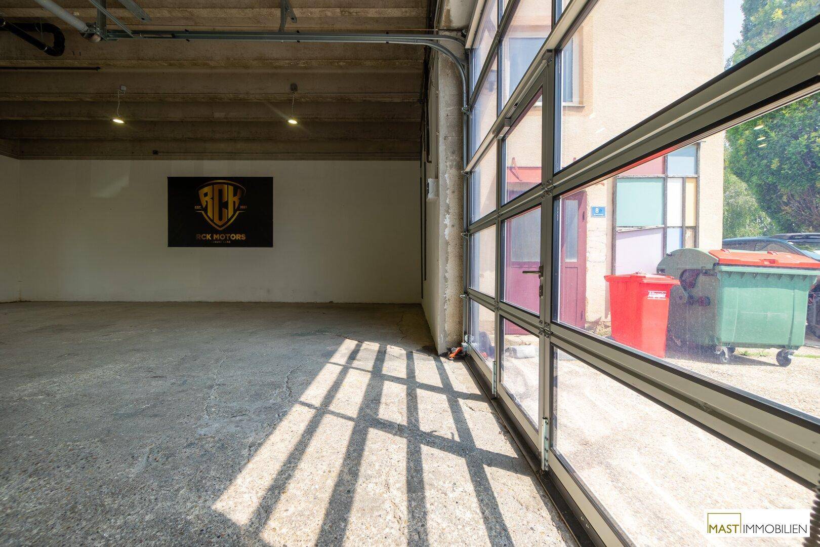 Blick aus der Lagerhalle durch ein großes Glasrolltor auf den Außenbereich und die Straße.