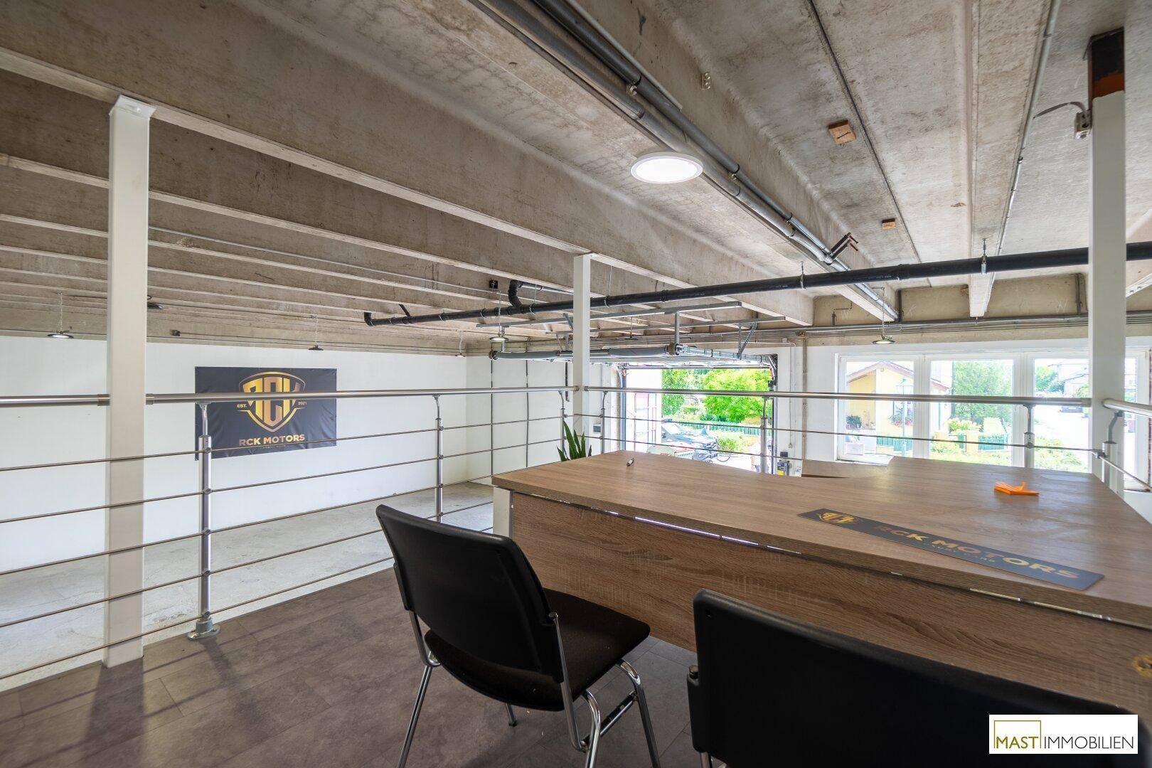 Büro auf einer Galerieebene in einer Lagerhalle mit Blick auf den Arbeitsbereich darunter.