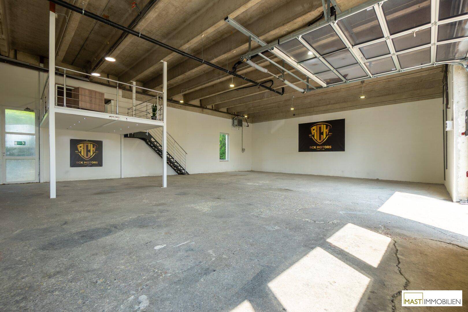 Weitläufige Lagerhalle mit Betonboden, hohen Decken und einer integrierten Galerie.