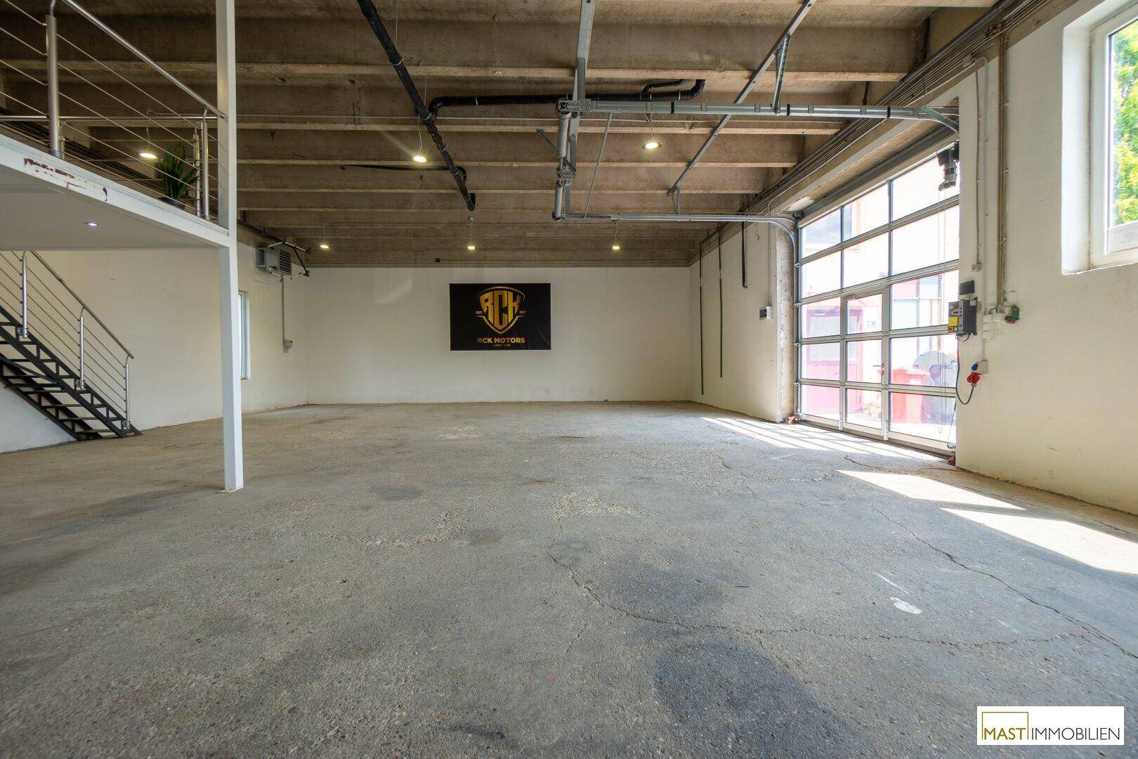 Große Lagerhalle mit Betonboden, hohen Decken und einem breiten Rolltor für den Zugang.