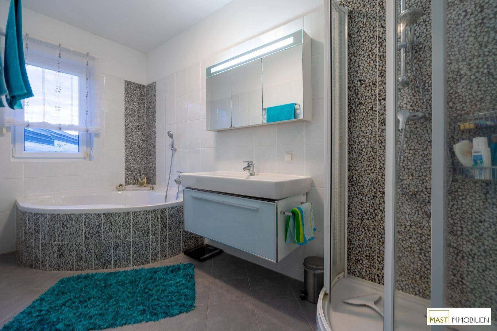 Helles Badezimmer mit Eckbadewanne, Duschkabine und Fenster für Tageslicht.