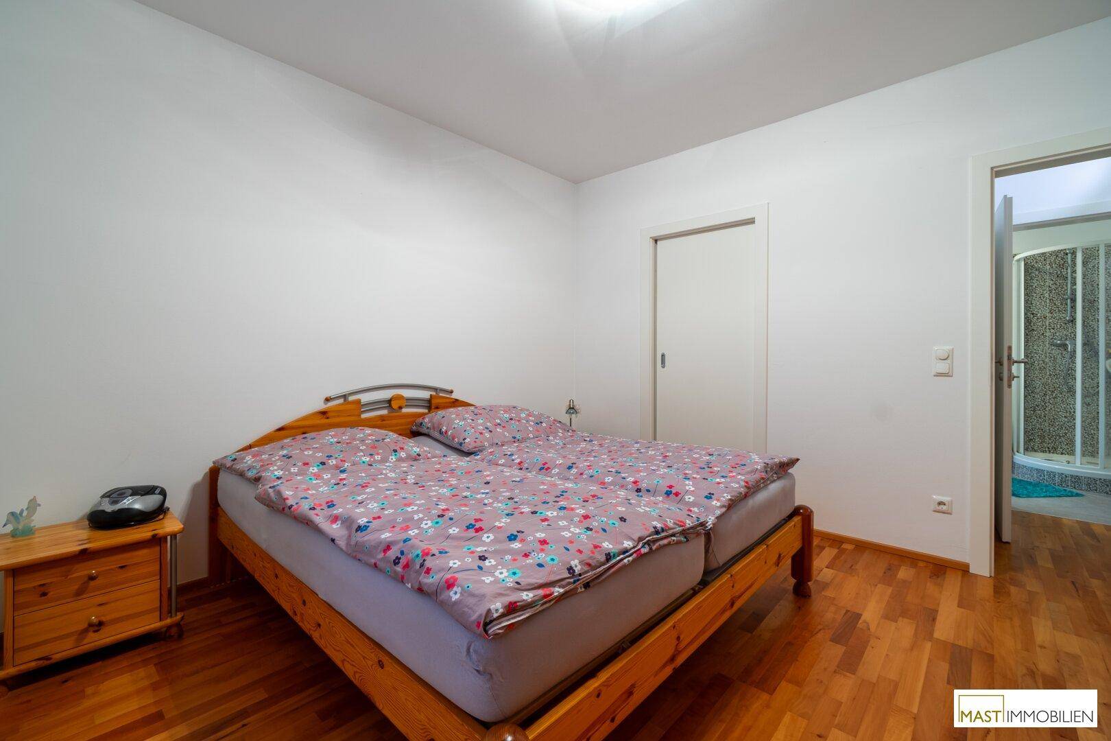Schlafzimmer mit Holzbett und direktem Zugang zum Badezimmer, mit Holzboden.
