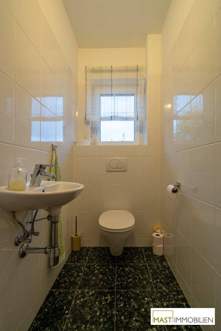 Separate Toilette mit Fenster, wandhängendem WC und kleinem Waschbecken.