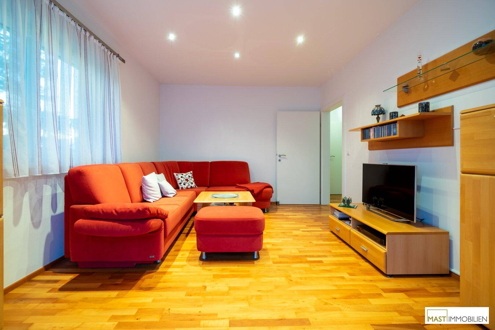 Helles Wohnzimmer mit großem rotem Ecksofa, Holzboden und TV-Möbeln.