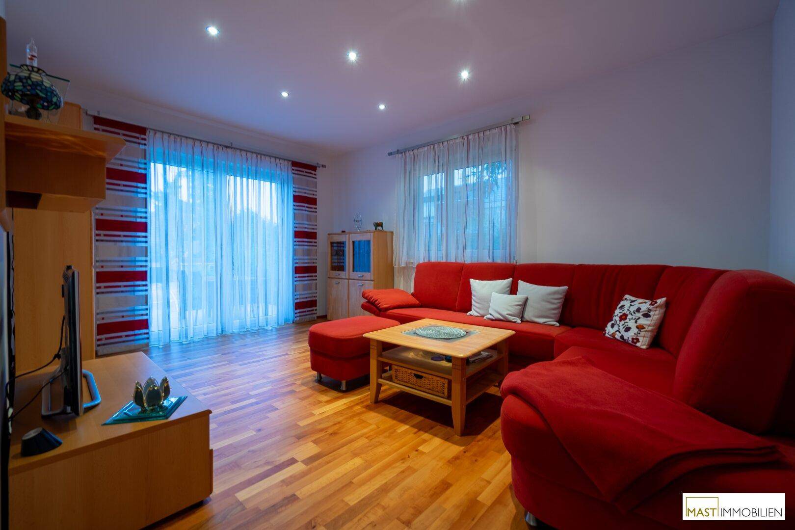 Gemütliches Wohnzimmer mit rotem Sofa, Holzboden und Zugang zum Außenbereich.