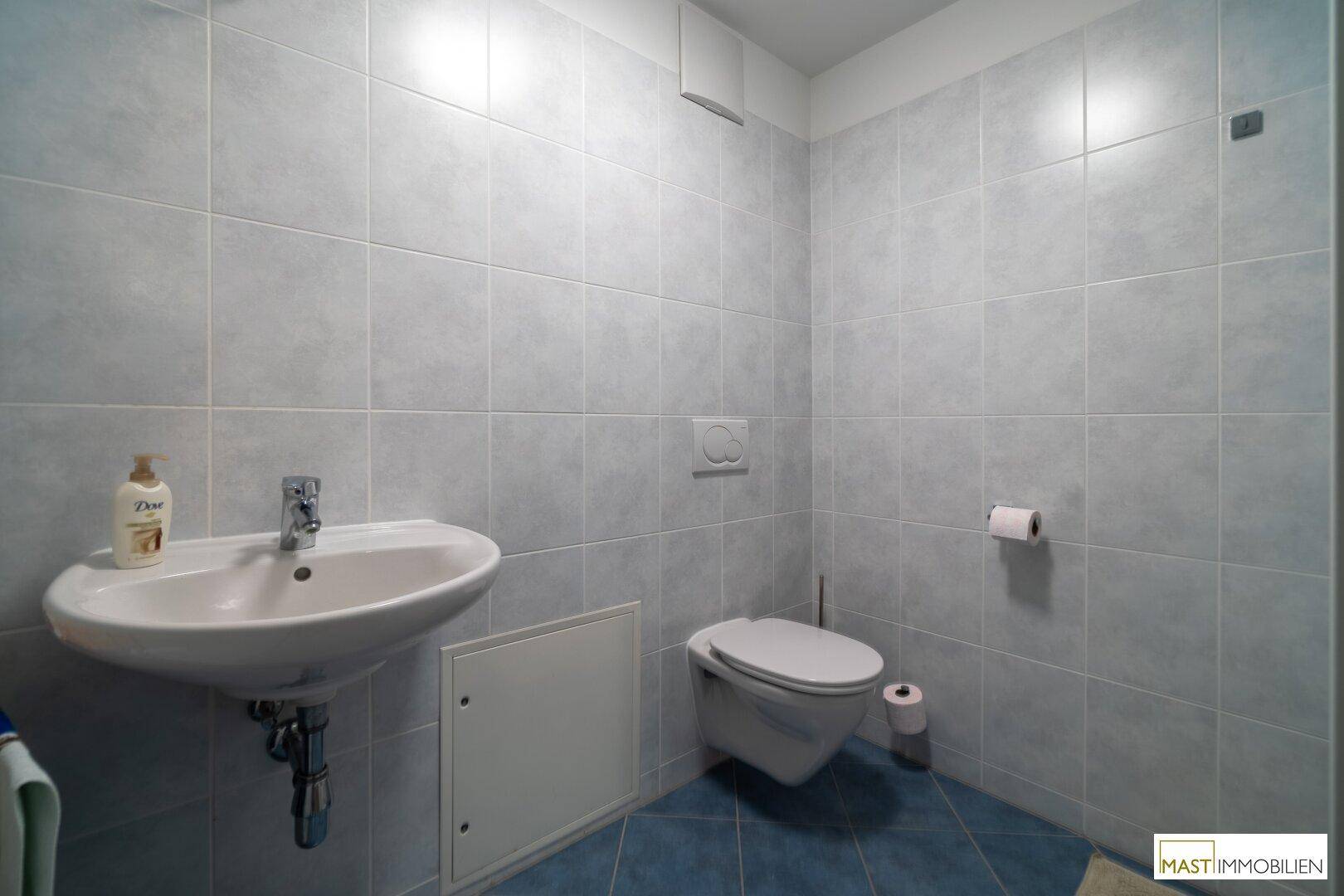 Kleines Gäste-WC mit Wand-WC und Waschbecken, hell gefliest.