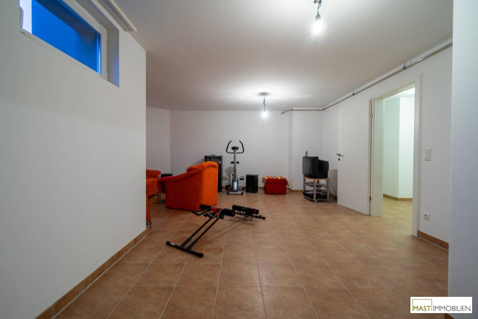 Geräumiger Fitnessraum im Keller mit Trainingsgeräten und Sitzgelegenheiten.