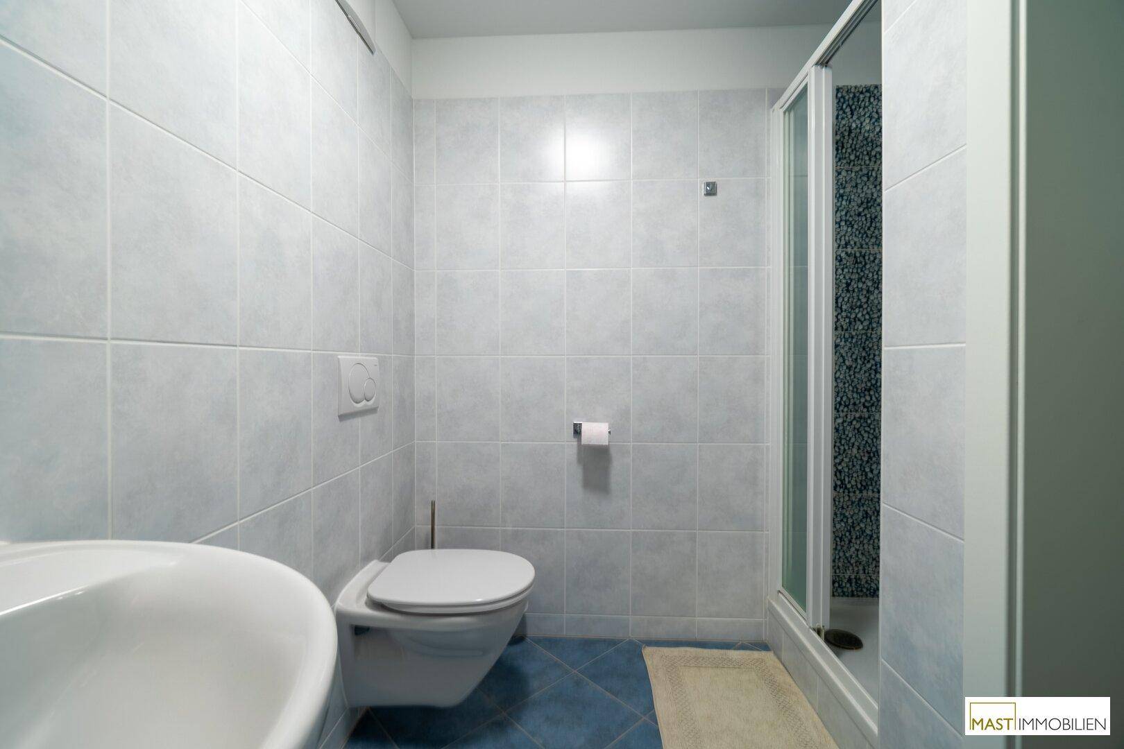 Badezimmer mit Dusche, WC und Waschbecken, komplett gefliest in hellen Farben.