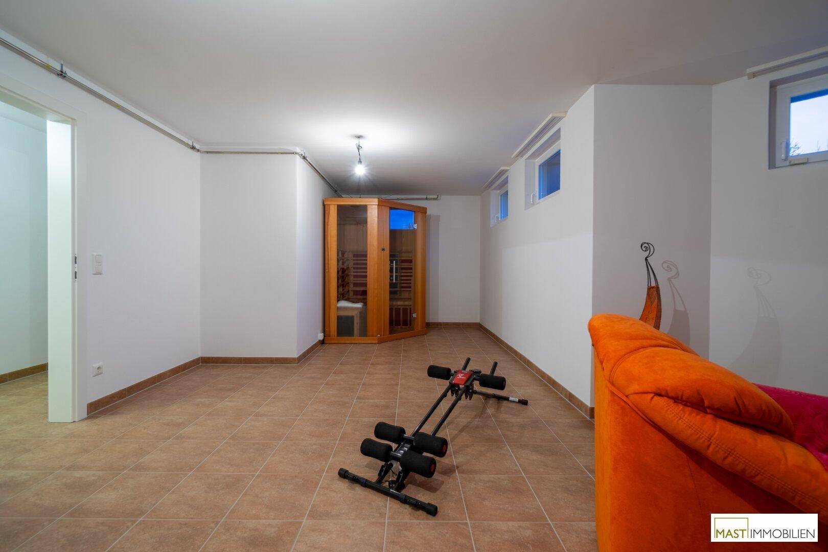 Großer Raum im Untergeschoss mit Sauna und Fitnessgeräten, ideal für Wellness und Sport.