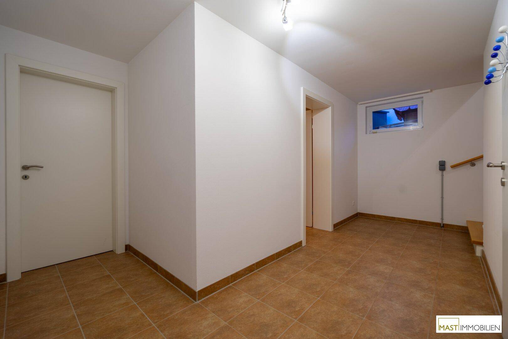 Kellerraum mit Fliesenboden, kleinem Fenster und Zugang zu weiteren Räumen.