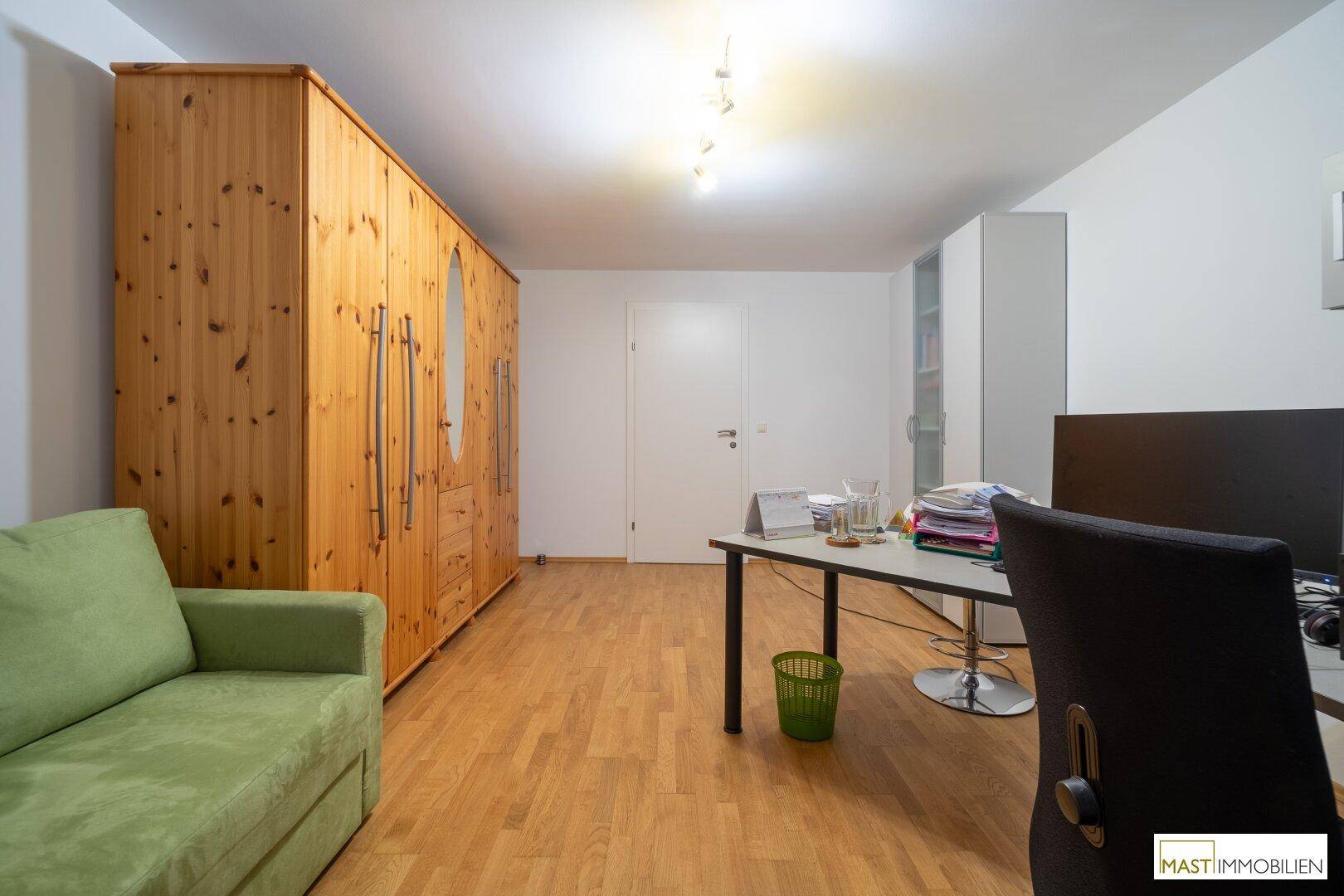 Geräumiges Zimmer mit Holzschrank, Schreibtisch und grünem Sofa, ideal als Büro oder Gästezimmer.