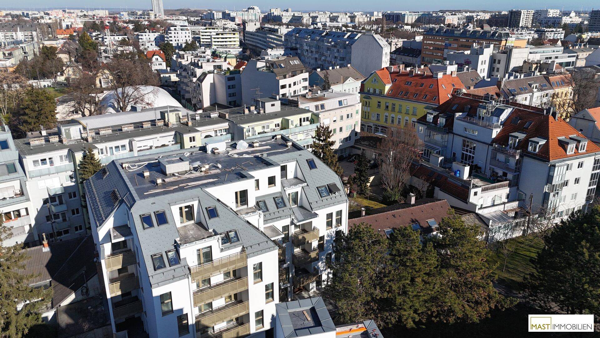 Luftaufnahme eines modernen Wohngebäudes mit Dachschrägen und Balkonen in einer städtischen Umgebung.