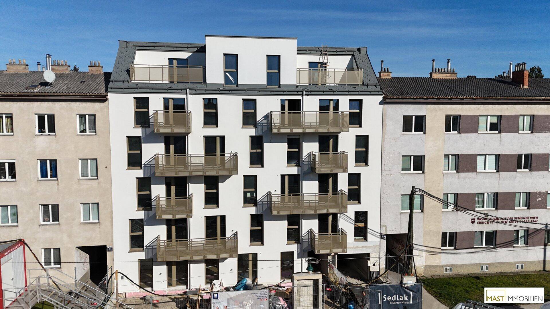 Modernes Mehrfamilienhaus mit weißer Fassade, vielen Balkonen und großen Fenstern in städtischer Umgebung.