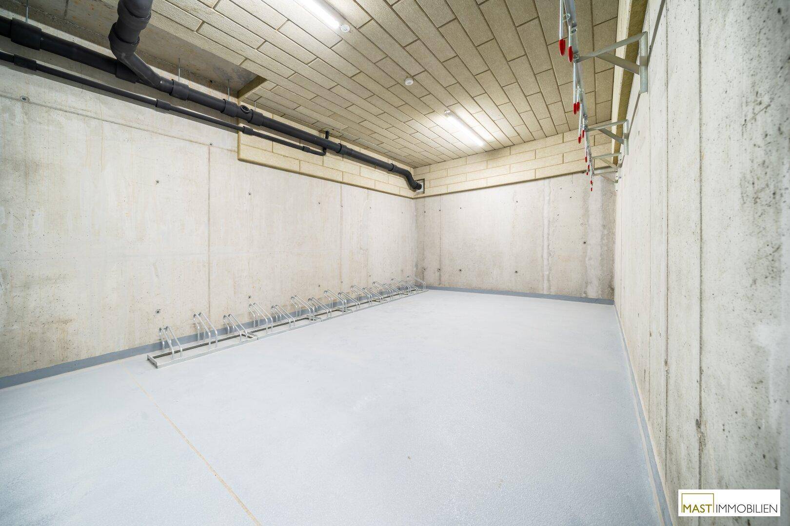 Heller Fahrradraum im Untergeschoss mit Betonwänden und praktischen Fahrradständern.