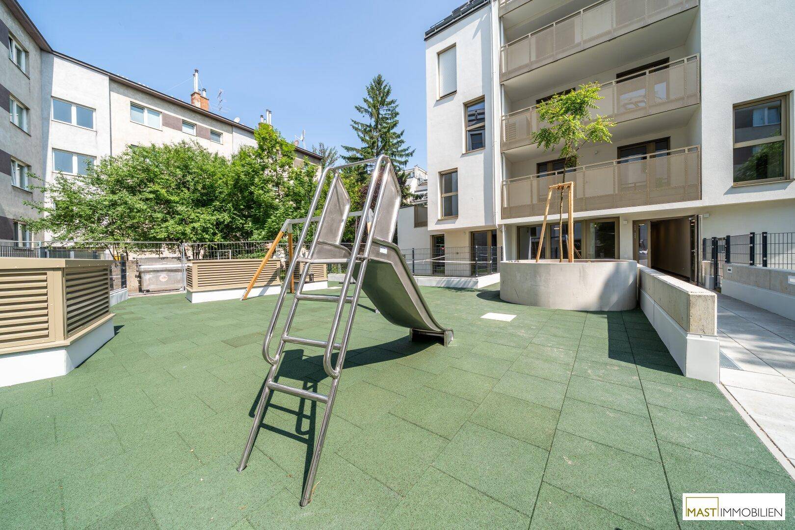 Spielbereich mit einer Rutsche und Blick auf die moderne Fassade des Wohngebäudes.