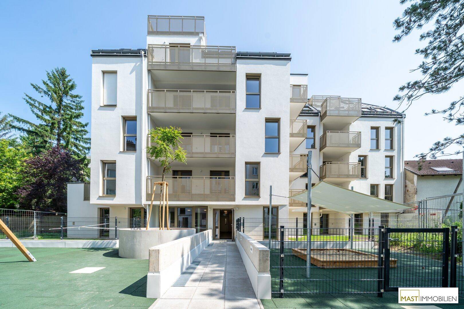 Neubau-Wohngebäude mit mehreren Balkonen und einem gut ausgestatteten Kinderspielplatz.