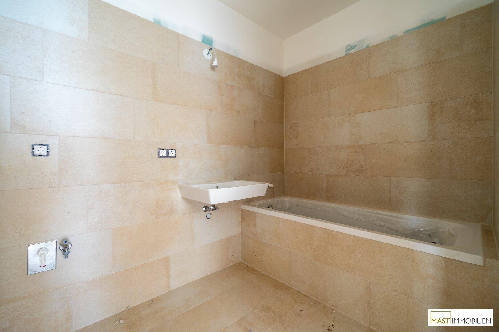 Modernes Badezimmer in Bauphase mit Badewanne, Waschbecken und beigefarbenen Fliesen.