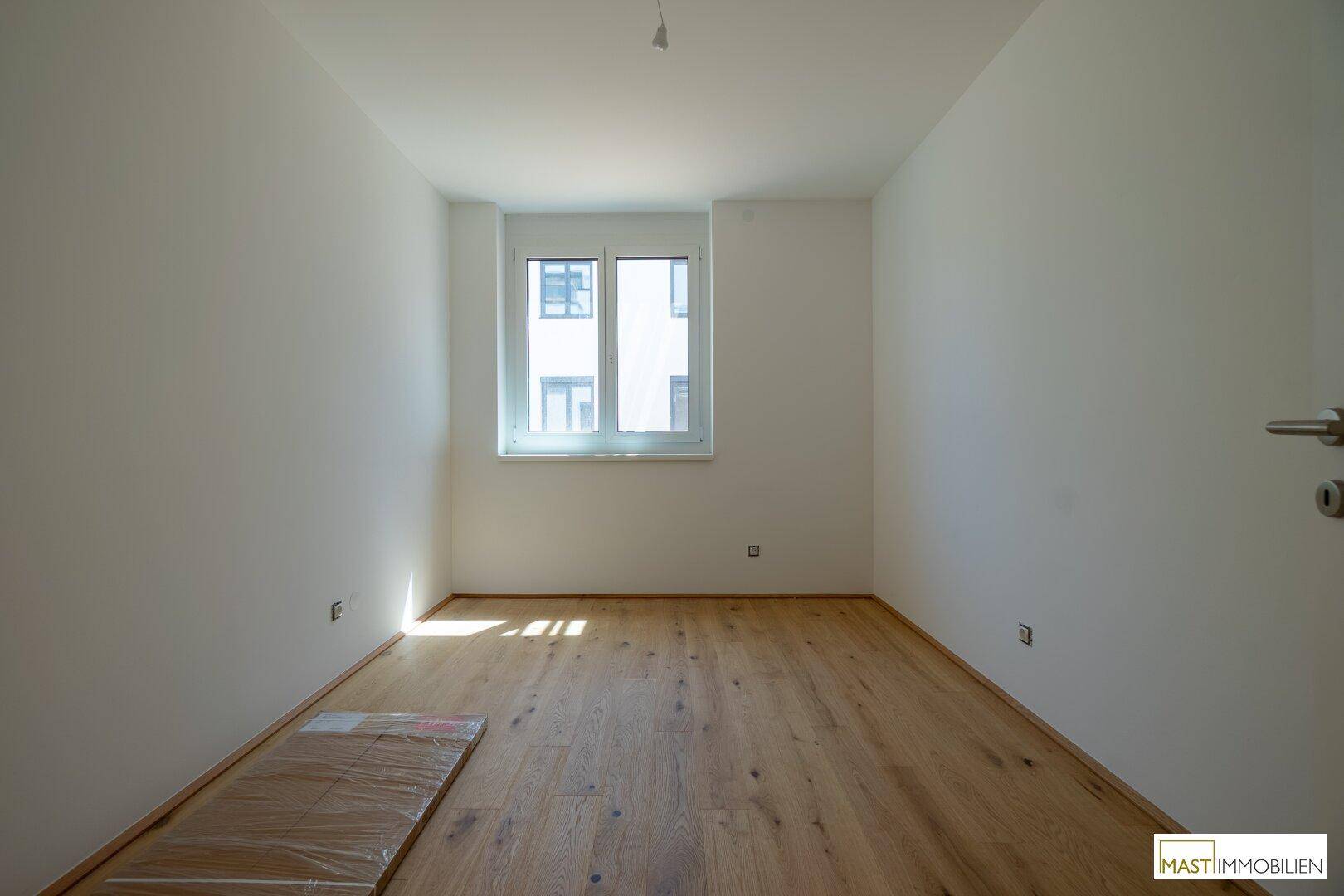 Unmöbliertes Zimmer mit Holzboden und einem großen Fenster, ideal als Schlaf- oder Arbeitszimmer.