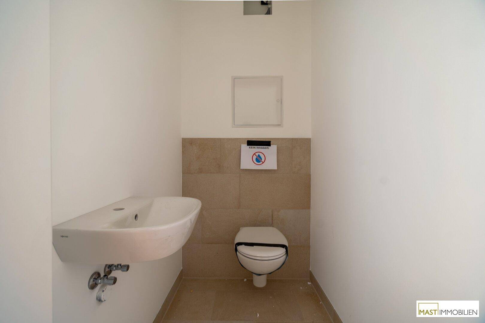 Funktionale Gästetoilette mit Wand-WC und kleinem Waschbecken in neutralen Farben.