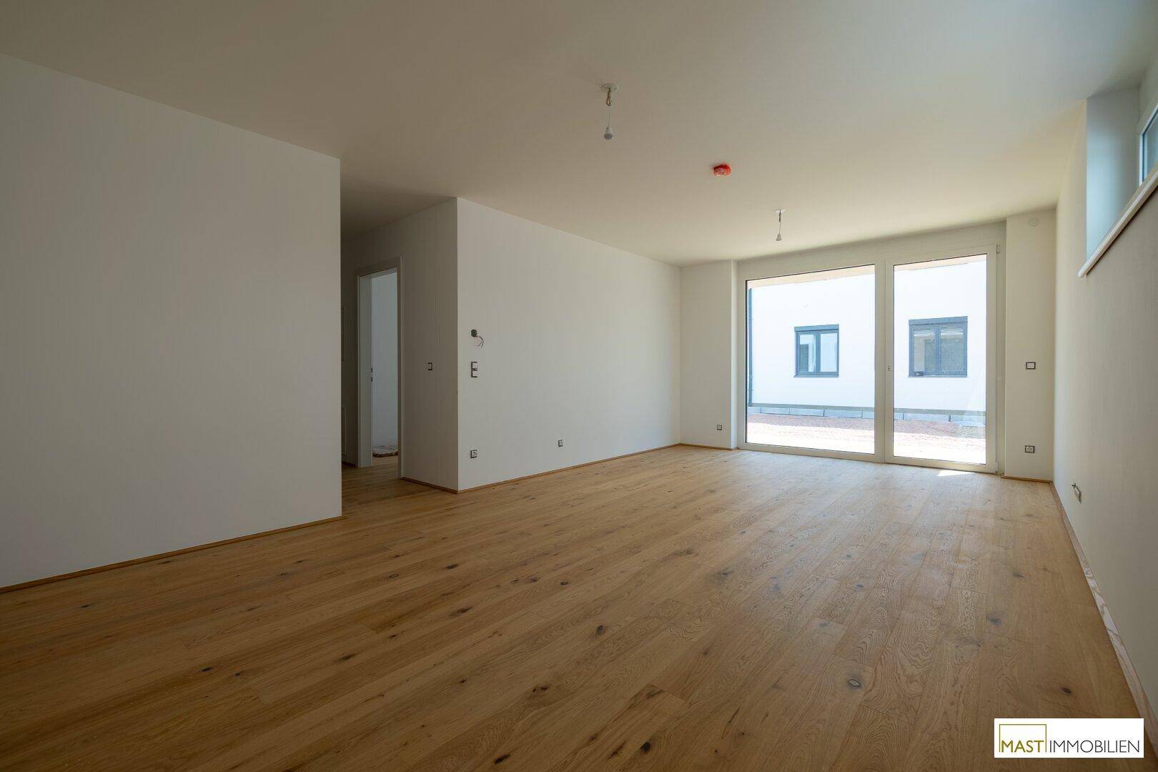 Geräumiges, unmöbliertes Wohnzimmer mit Holzboden und viel Tageslicht durch große Fenster.