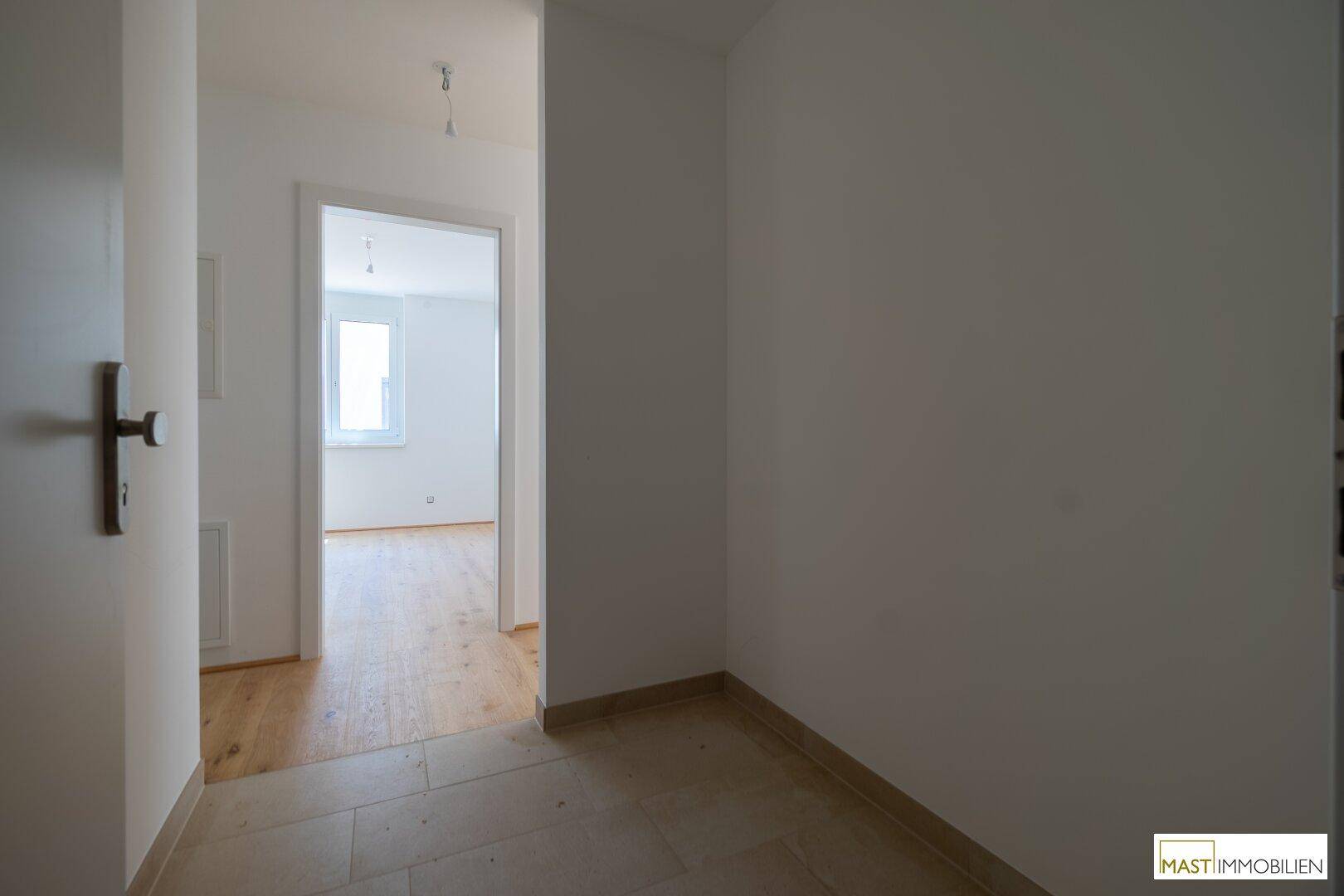Heller Flur mit Fliesenboden, der zu weiteren Zimmern mit Holzboden führt.