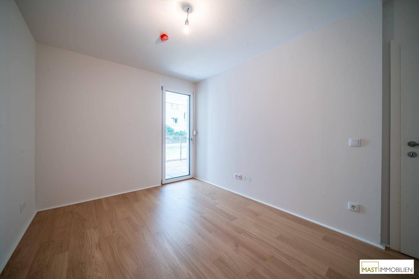 Lichtdurchflutetes Zimmer mit Parkettboden und weiß gestrichenen Wänden, ideal als Schlafzimmer.