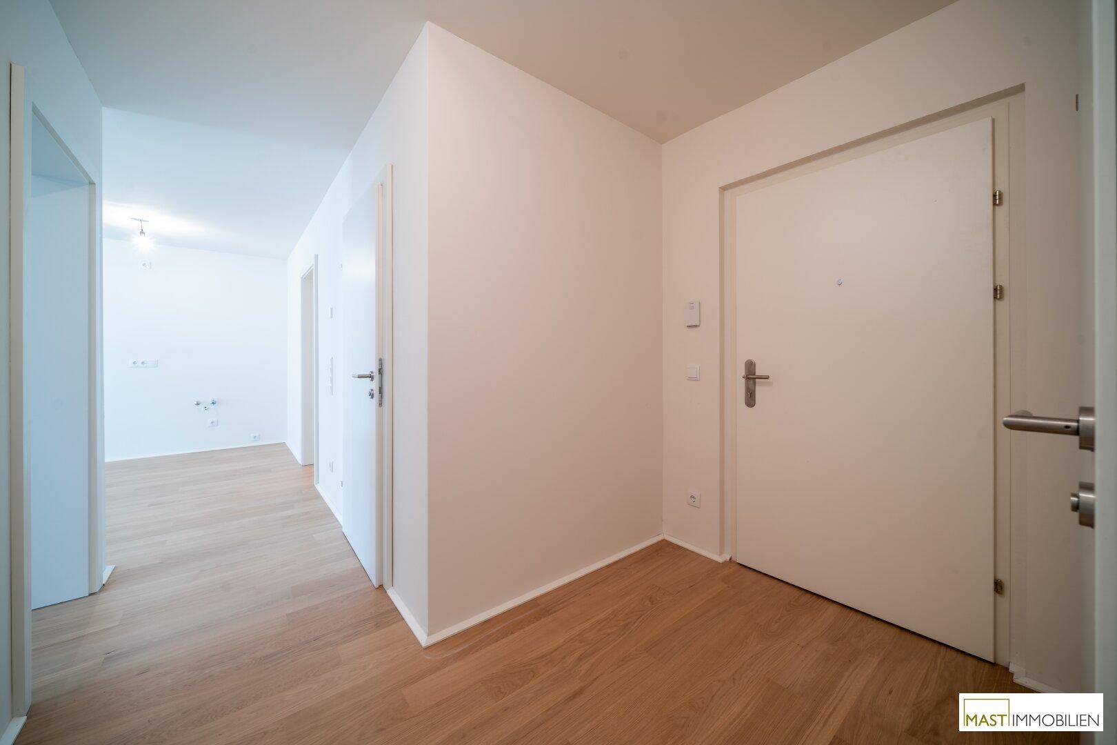 Heller Flur mit Holzboden und weißen Wänden, der zu verschiedenen Räumen führt.