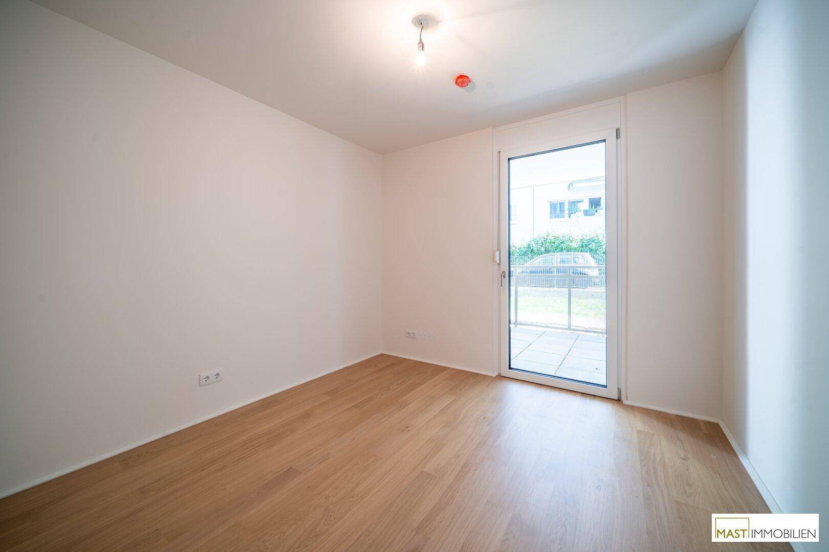 Helles Zimmer mit Holzboden und weiß gestrichenen Wänden, mit Zugang zu einem kleinen Außenbereich.