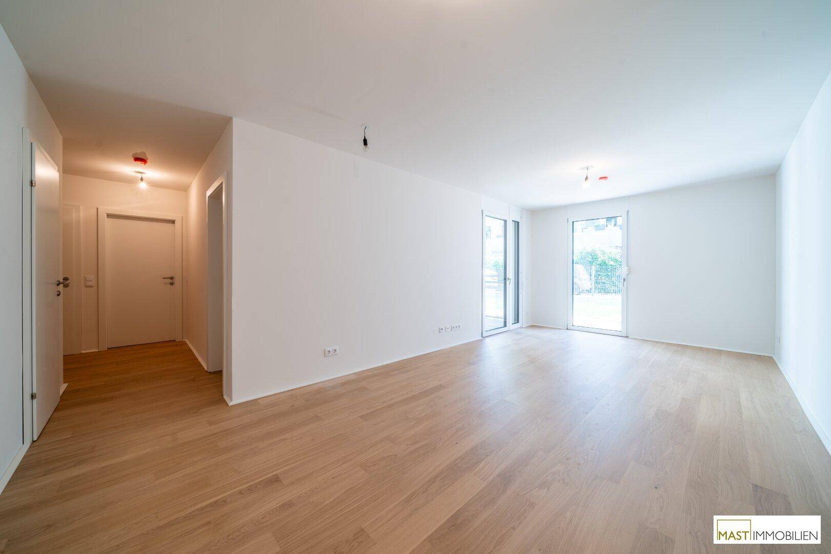 Helles, leeres Zimmer mit hellem Parkettboden und Zugang zu einem Außenbereich.