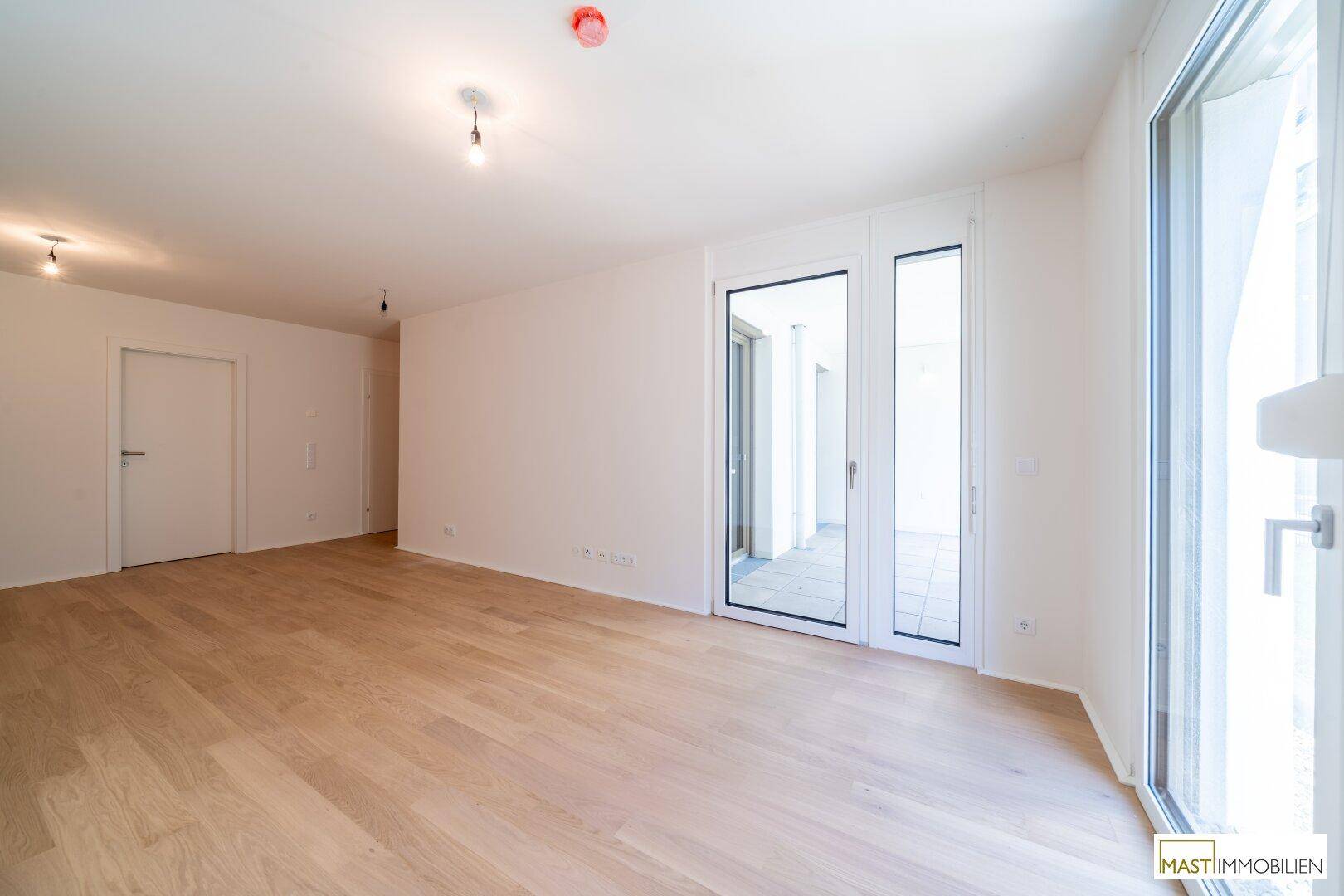 Geräumiges, helles Zimmer mit Holzboden und großem Fenster mit Zugang zum Außenbereich.