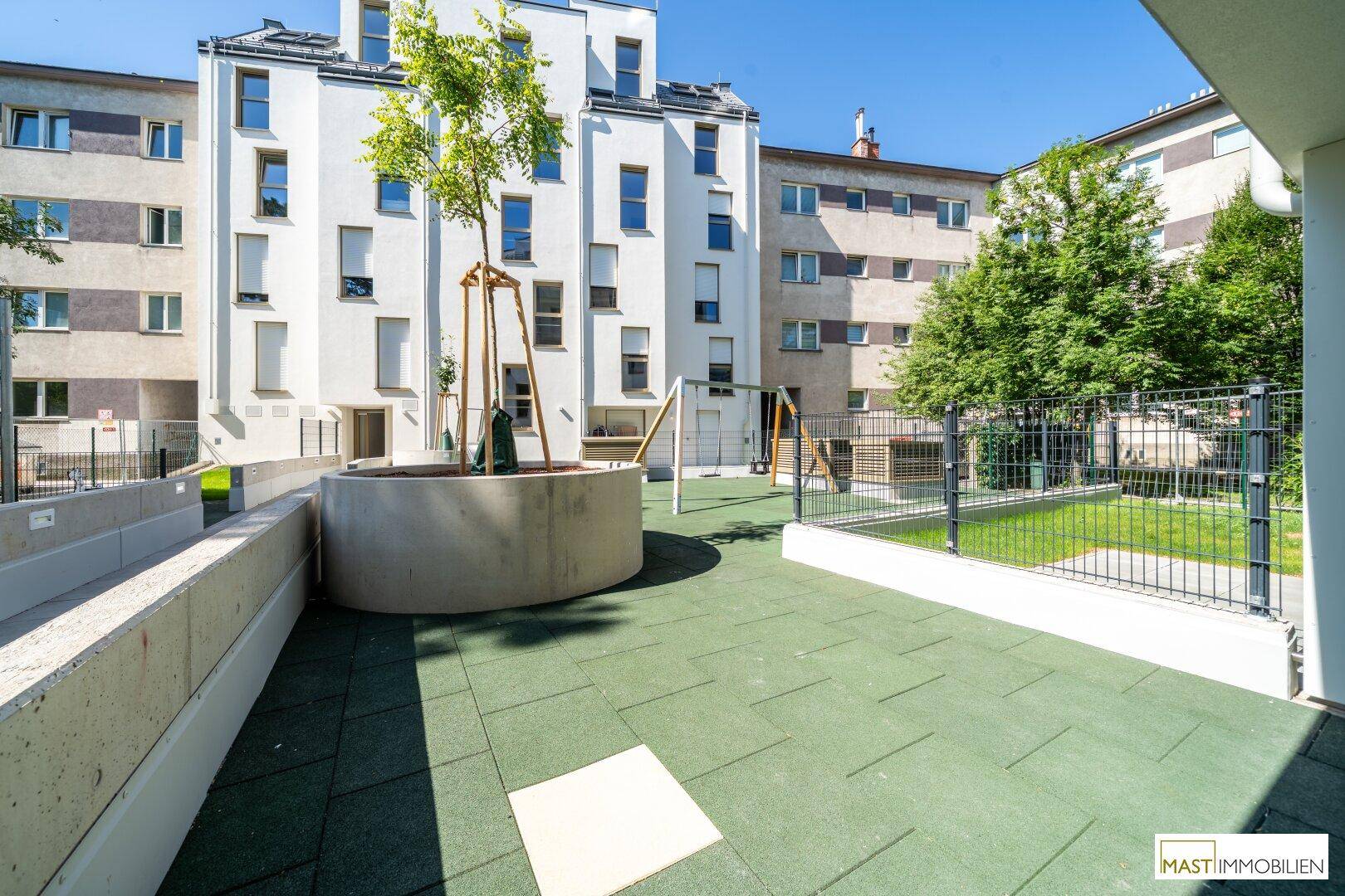 Gemeinschaftlicher Spielplatz mit Grünflächen und Spielgeräten im Innenhof der Wohnanlage.