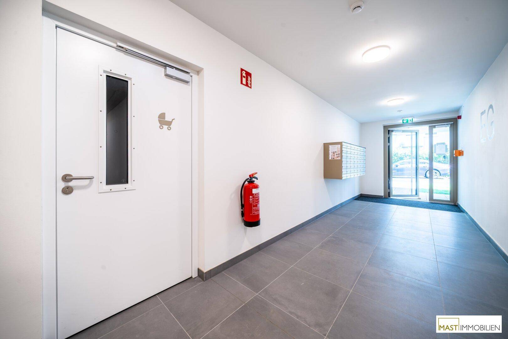 Geräumiger Flur mit Fliesenboden, Brandschutzvorrichtungen und Zugang zum Außenbereich.