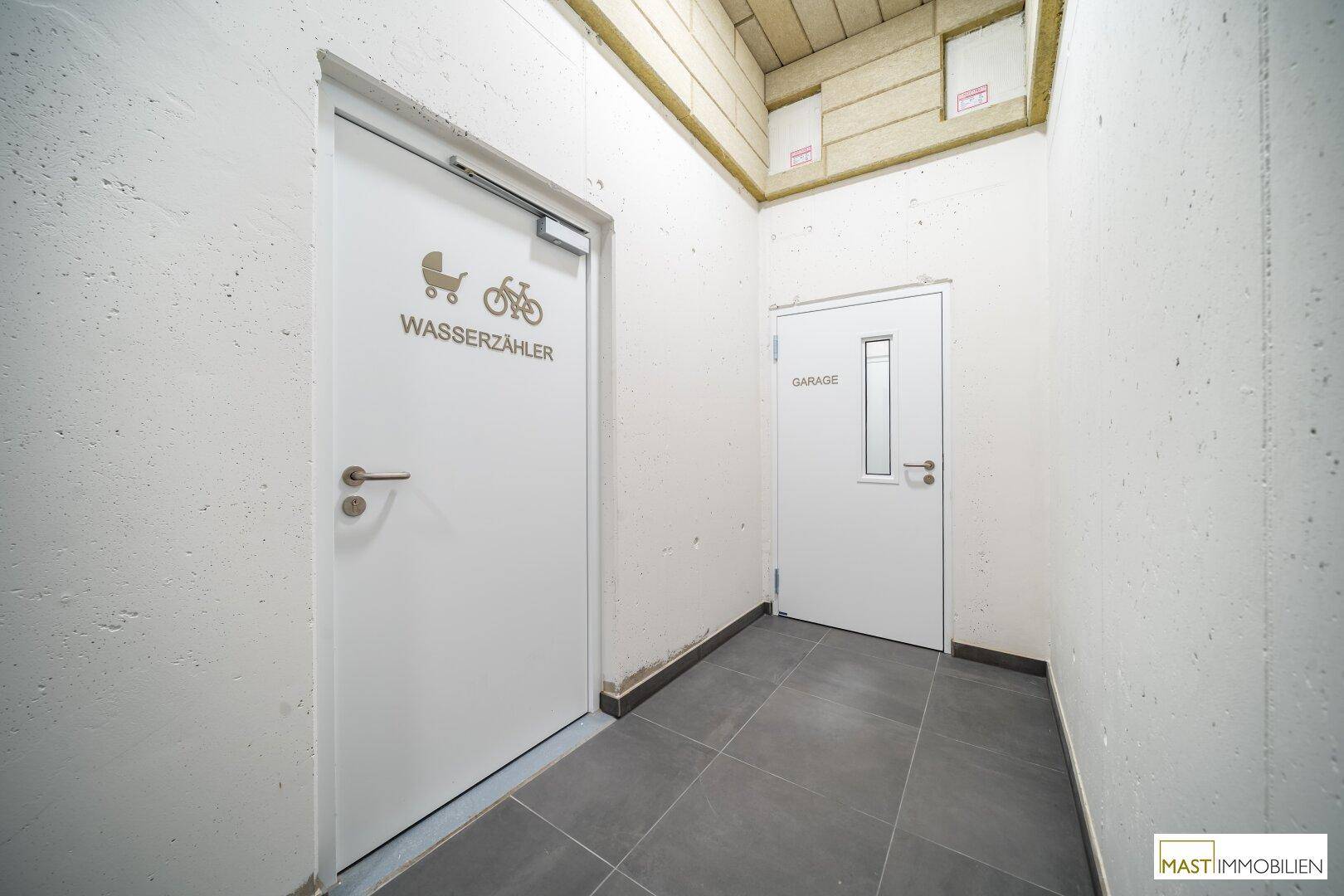 Kellerflur mit Türen zu verschiedenen Räumen, darunter Wasserzähler und Garage.