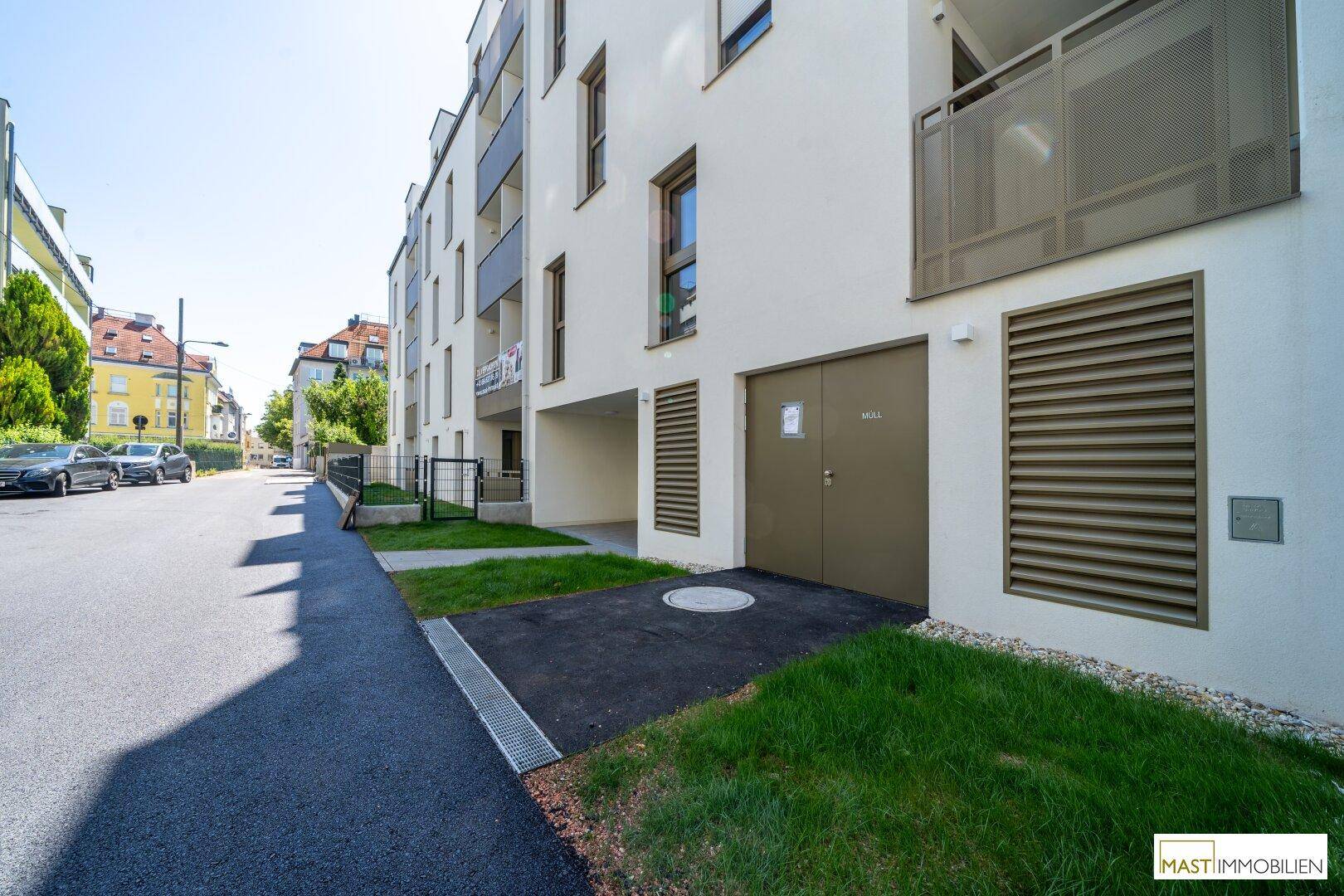 Moderne Wohnanlage mit weißer Fassade und begrüntem Eingangsbereich an einer ruhigen Straße.