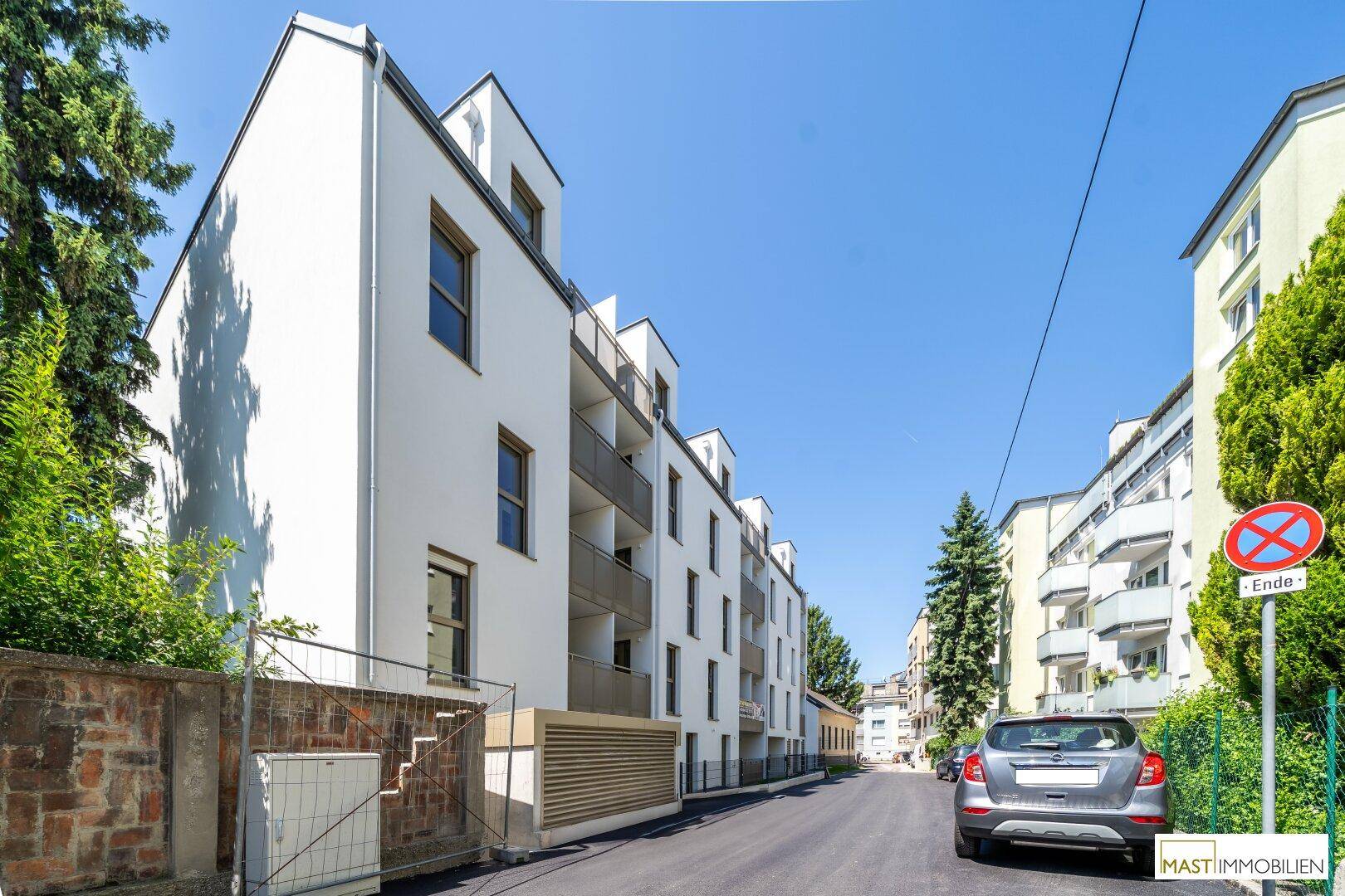 Moderne Wohnanlage mit weißer Fassade und Balkonen, umgeben von Bäumen und einer ruhigen Straße.