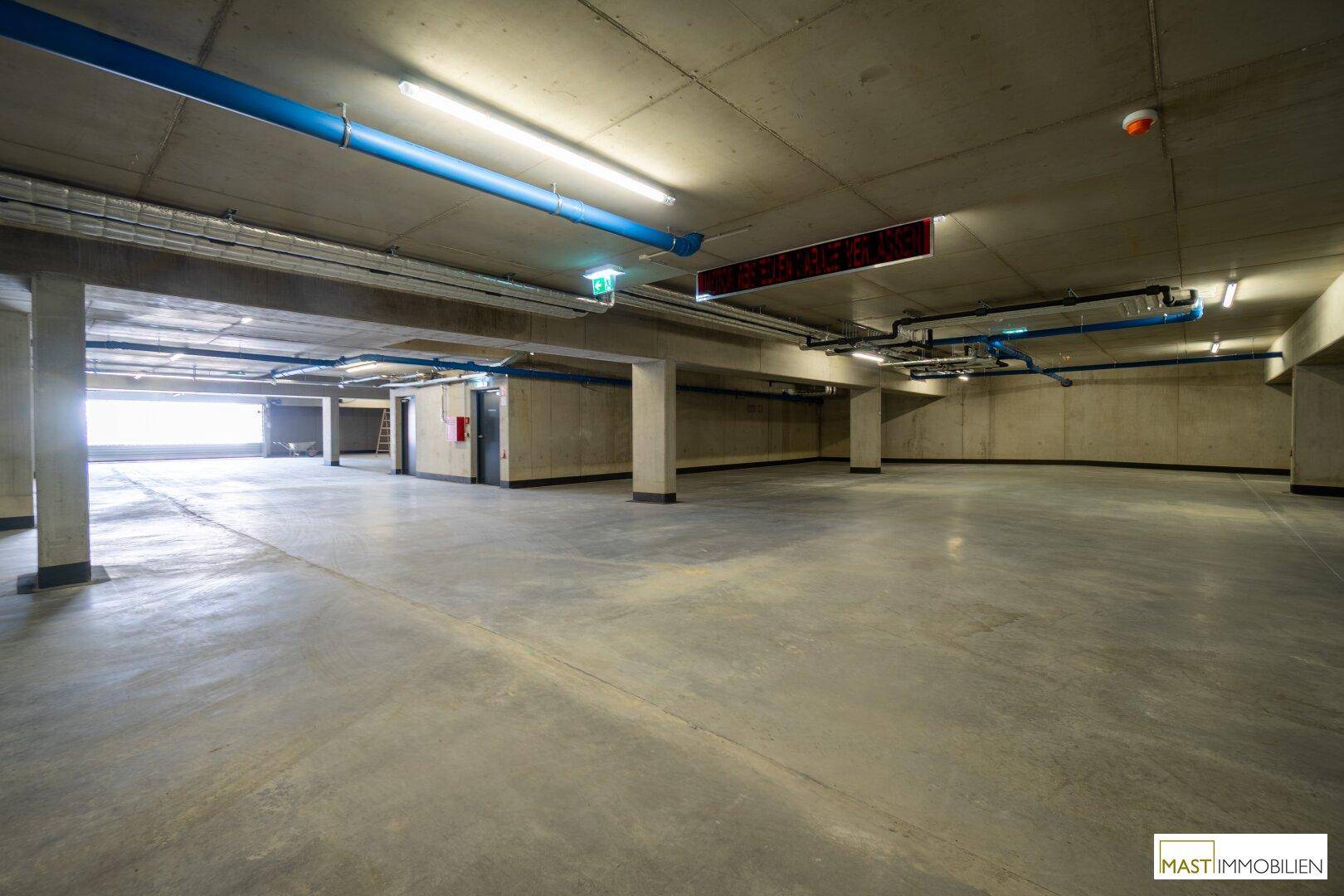 Geräumige Tiefgarage mit Betonboden und sichtbaren Installationen, bietet viel Platz.