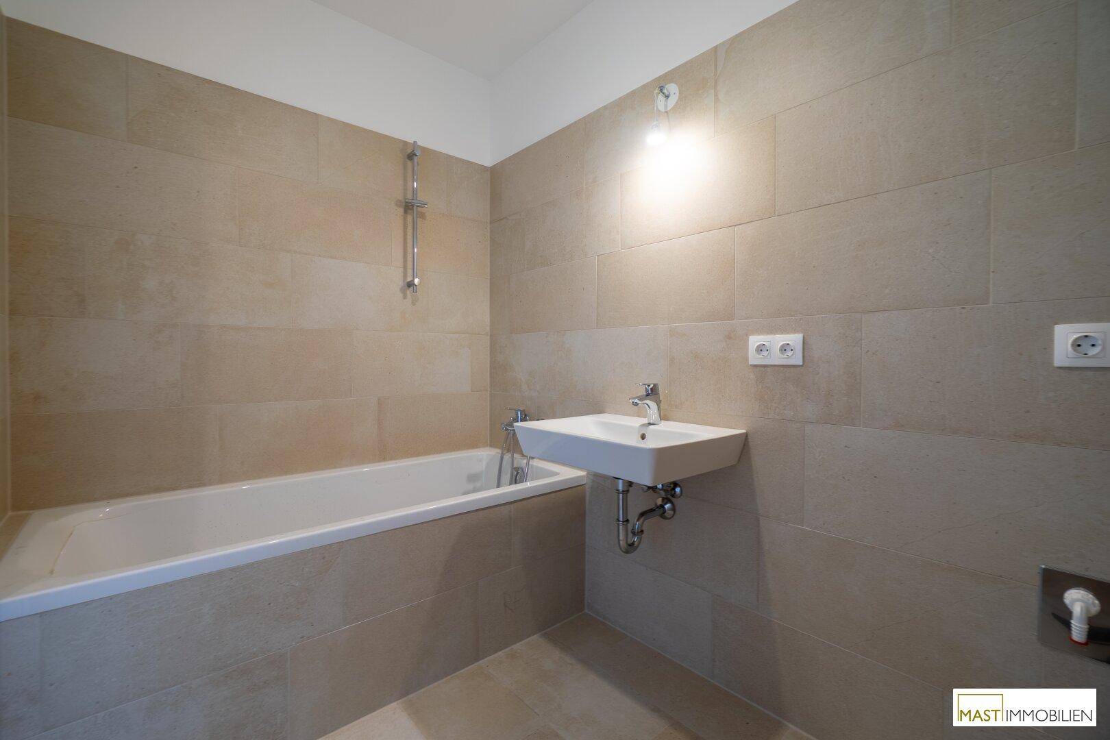 Modernes Badezimmer mit Badewanne, Einzelwaschbecken und beigefarbenen Wandfliesen.